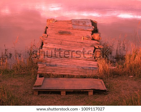 Old red fishing wooden pier and river against the backdrop of mountains and colorful sunset. Meditative relaxing natural landscape