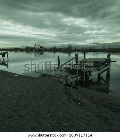 Old grey fishing pier, clouds, mountains, river, field, shore and colorful sunset. Silence and immense beauty. Country Romance