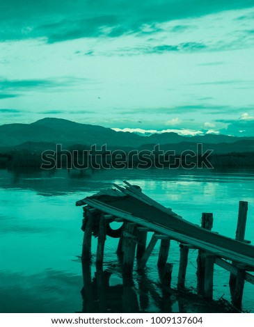 Old aqua colored fishing pier, clouds, mountains, river, field, shore and colorful sunset. Silence and immense beauty. Country Romance