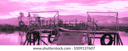 Pink sunset and old fishing wooden pier and river on a background of mountains. Meditative relaxing natural landscape