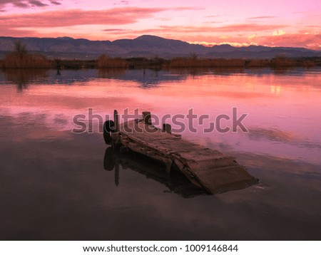 Old red fishing wooden pier and river against the backdrop of mountains and colorful sunset. Meditative relaxing natural landscape