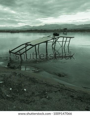 Old grey fishing pier, clouds, mountains, river, field, shore and colorful sunset. Silence and immense beauty. Country Romance