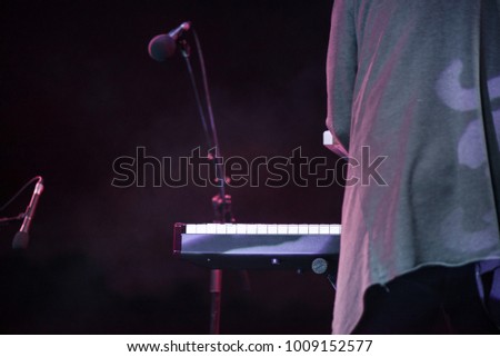 Male musician plays a musical instrument on the stage. Artist playing on the keyboard synthesizer piano keys. Live concert of electronic music at night in summer festival. Colorful, abstract lights