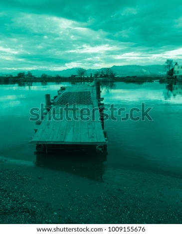 Old aqua colored fishing pier, clouds, mountains, river, field, shore and colorful sunset. Silence and immense beauty. Country Romance