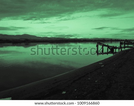 Green sunset and old fishing wooden pier and river on a background of mountains. Meditative relaxing natural landscape