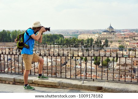 man traveler in a hat with a backpack and camera admiring the view of the city of Toledo from the observation deck