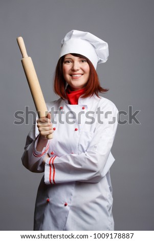 Picture of woman cook in white robe and cap with rolling pin in hands