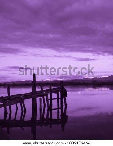 Old violet colored fishing pier, clouds, mountains, river, field, shore and colorful sunset. Silence and immense beauty. Country Romance