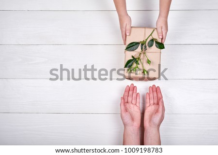 Son giving gift box with flowers to mum, top view. Holidays, present, childhood concept. Close up of child and mother hands with gift box on white background. Mothers day, Womans day (March 8)