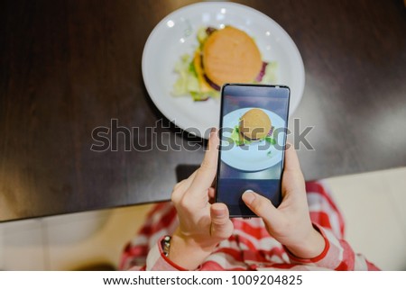 woman take picture of hamburger on her phone to share it after in social networks
