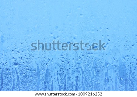 Frozen glass of the window from the inside of the room. Background in a cool tone with a texture of dripping water drops