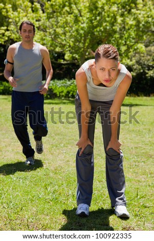 Woman bending over to recover while a man is jogging close to her in the background