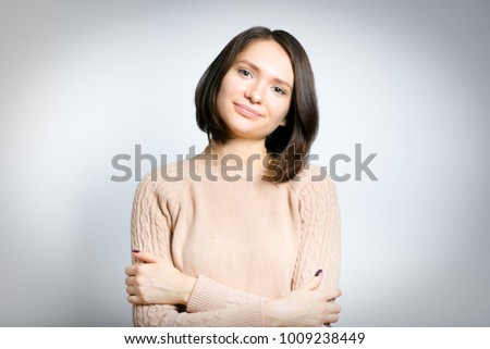portrait of a young tender woman hugging herself cozy, wearing a pink sweater, isolated on background, studio photo