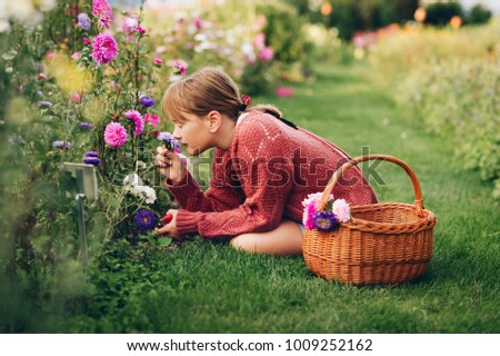 Pretty little girl working in autumn garden, child taking care of colorful chrysanthemum, gardener teenager enjoying warm and sunny day Royalty-Free Stock Photo #1009252162