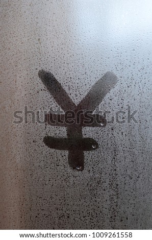 Chinese Yen Symbol is written with a finger on the surface of the misted glass