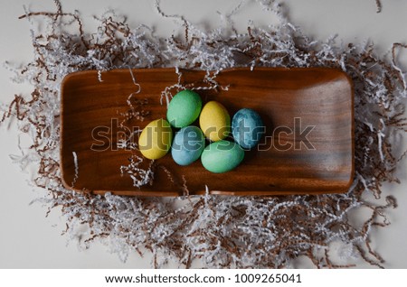 Colorful easter eggs in a vintage and rustic wooden tray, with paper grass and a white background. From above / flat lay style.