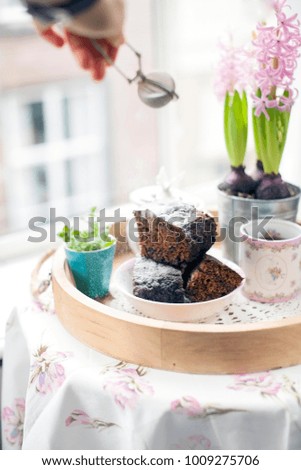 Homemade chocolate cake for breakfast, on the table by the window. View from the window to the city. Flowers and fragrant coffee. Free space for text or a postcard. Hand in the frame.