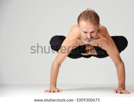 Old man practicing yoga classic asana dance pose standing on hands against white background