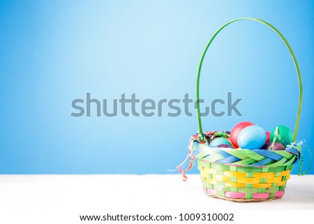 Photo of basket with colorful eggs on empty blue background.