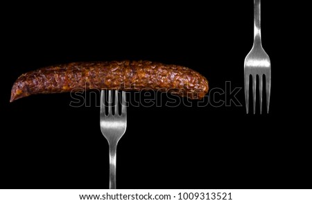 Tasty big sausage stuck on a silver fork isolated on a black background Royalty-Free Stock Photo #1009313521
