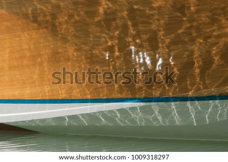 Sun reflecting off the surface of water onto the side of wooden boat that has a white bottom and teal waterline.