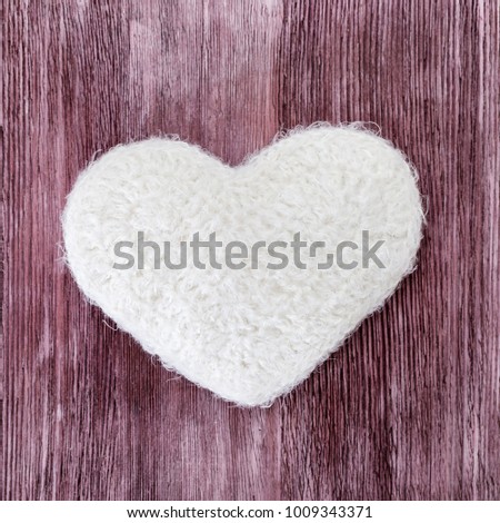 Hand knitted white heart on a wood texture background. The figure of the heart is connected with white thread. Flat lay.
