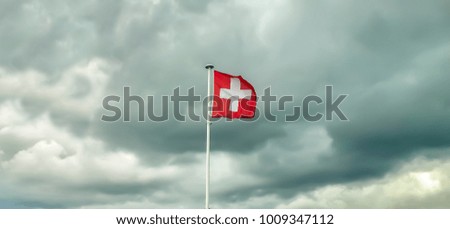 Swiss flag blowing in front of grey cloudy sky