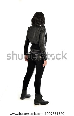 full length portrait of black haired girl wearing leather outfit, standing pose facing away from camera.  isolated on white background. Royalty-Free Stock Photo #1009361620