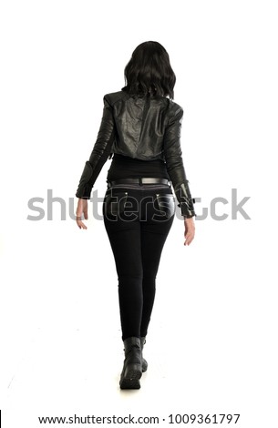 full length portrait of black haired girl wearing leather outfit, standing pose facing away from camera.  isolated on white background.