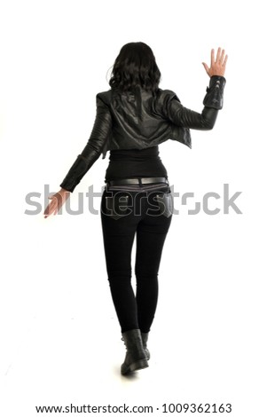 full length portrait of black haired girl wearing leather outfit, standing pose facing away from camera.  isolated on white background.