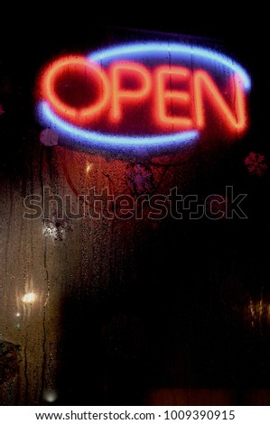 Glowing neon lighted red and blue open sign on business,
 seen through rain wet window at night
