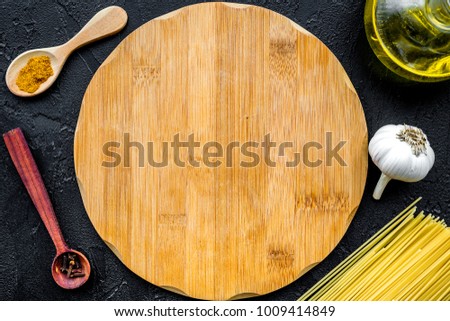 In restaurant. Mock up for menu or recipe. Wooden cutting board near ingredients. Raw pasta, oil, garlic, spices on black background top view