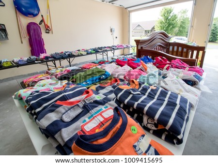Tables full of dishes, toys, and children's clothing for sale at a typical American garage sale Royalty-Free Stock Photo #1009415695