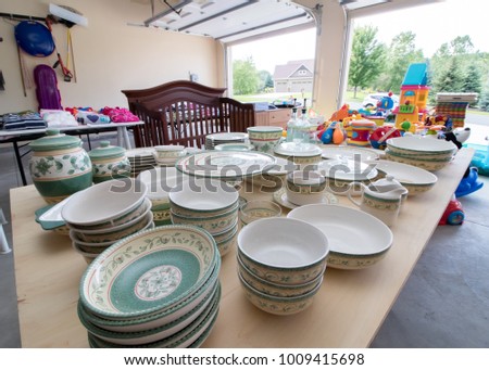 Tables full of dishes, toys, and children's clothing for sale at a typical American garage sale Royalty-Free Stock Photo #1009415698