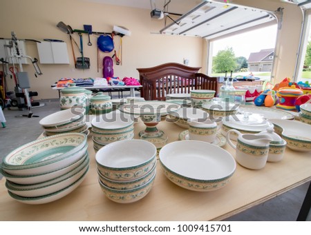 Tables full of dishes, toys, and children's clothing for sale at a typical American garage sale Royalty-Free Stock Photo #1009415701