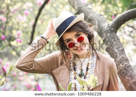 Happy girl rejoices in the spring garden. A girl dressed in boho style. Street fashion. Girl on nature. Accessories, sunglasses, necklaces, bracelets, watches, hat.