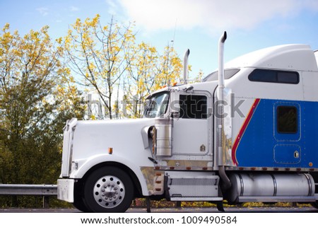 Profile of American idol popular big rig white and blue semi truck with high exhaust pipes and another chrome accessories and big comfortable rest cab for long haul freights going on the autumn road