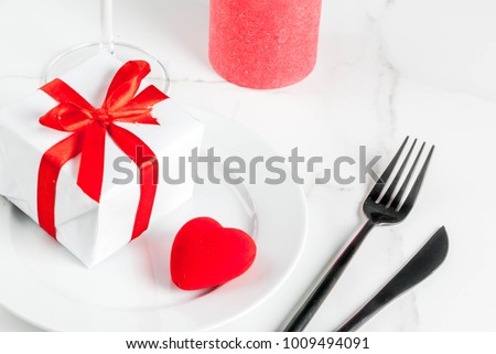 Valentine's day table setting with plate, fork, knife, gift box and red heart, on white marble background copy space