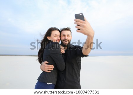 couple test camera in new smartphone, boyfriend and girlfriend taking selfies. Fellow in black shirt and girl in suit posing for photo. Concept of innovative technologies, using gadgets to m