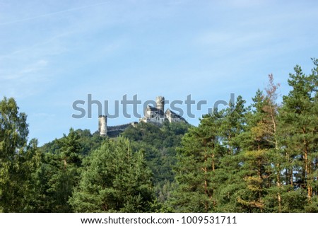 Panoramic view of Bezdez castle  with big tower in the Czech Republic. In the foreground there are trees, in the background is a hill with castle and there are a white clouds in the blue sky.