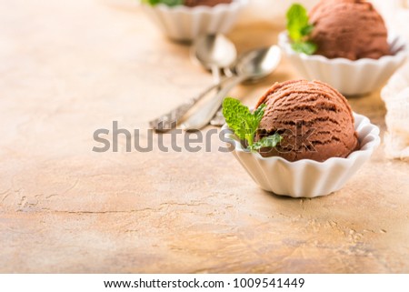 Chocolate ice cream scoop in white bowl with mint leaves on sand color stone background. Summer food concept with copy space.