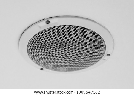 White round circle speaker and grille hanging on white ceiling. Selective focus