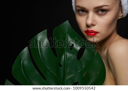 young woman with a palm leaf on a black background and a white towel on her head, beauty                               