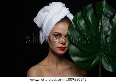 young woman with a palm leaf on a black background and a white towel on her head, beauty                               