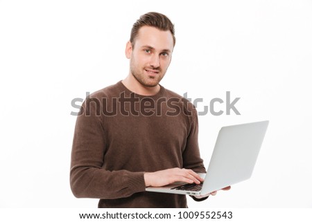 Image of smiling young man standing isolated over white background. Looking camera using laptop computer.