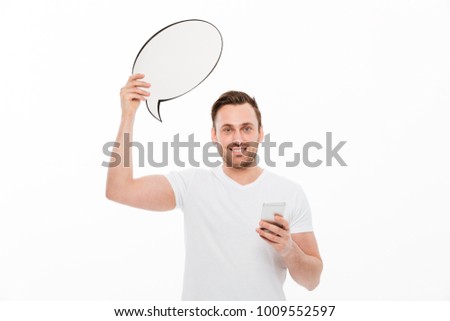 Picture of young man standing isolated over white background holding speech bubble using phone while looking camera.