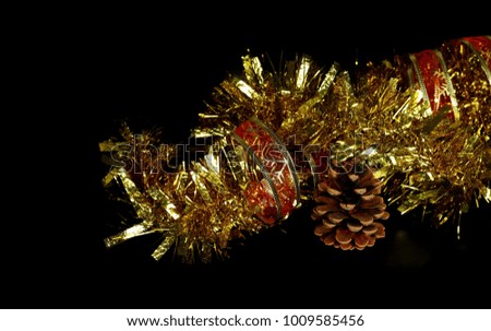 Golden, yellow tinsel, Christmas ornament, decoration with red ribbon and pine cone isolated on black background
