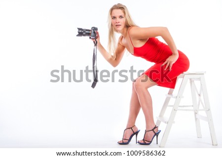 Girl with a camera. Blonde girl in a red dress. Girl photographer takes pictures. Girl learn to photograph. The camera is in the hands of a blonde.