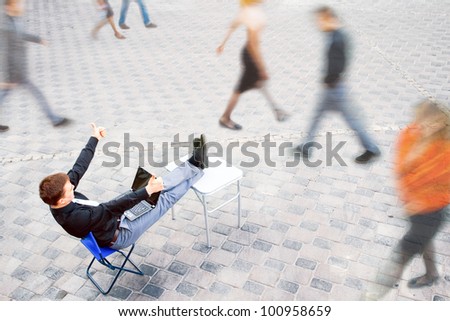 The image on top of a businessman sitting at the table in the street, which works with the computer and has a success.