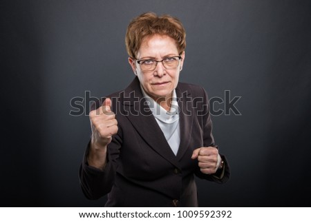 Business senior lady holding fists like fighting on black background